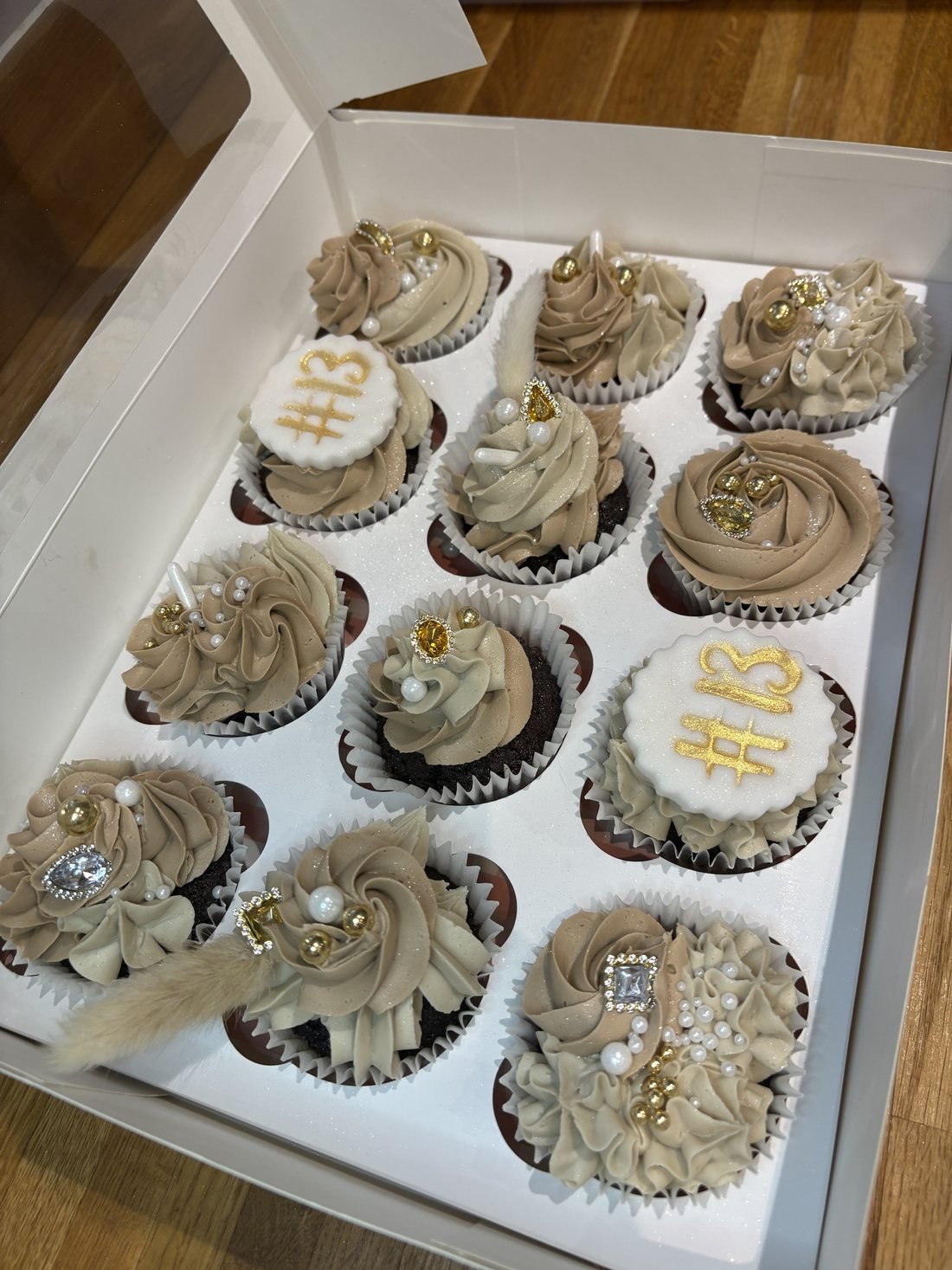 Box of twelve nude and gold chocolate cupcakes with jewels, pearls, bunny tail grass and #13 toppers