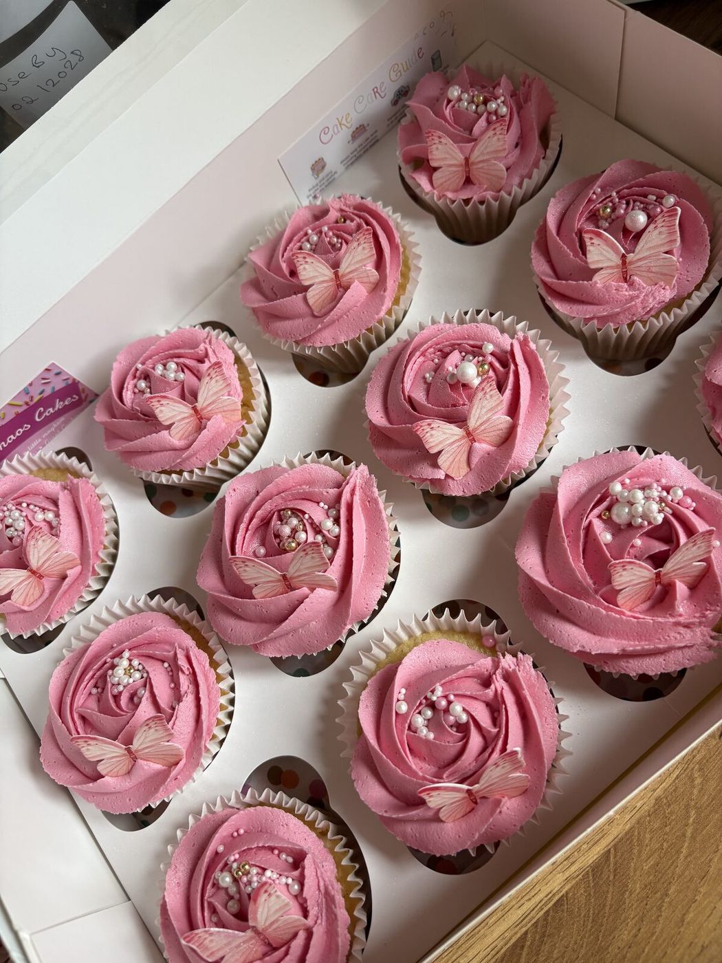 Box of pink rose swirl cupcakes with edible butterflies and pearls