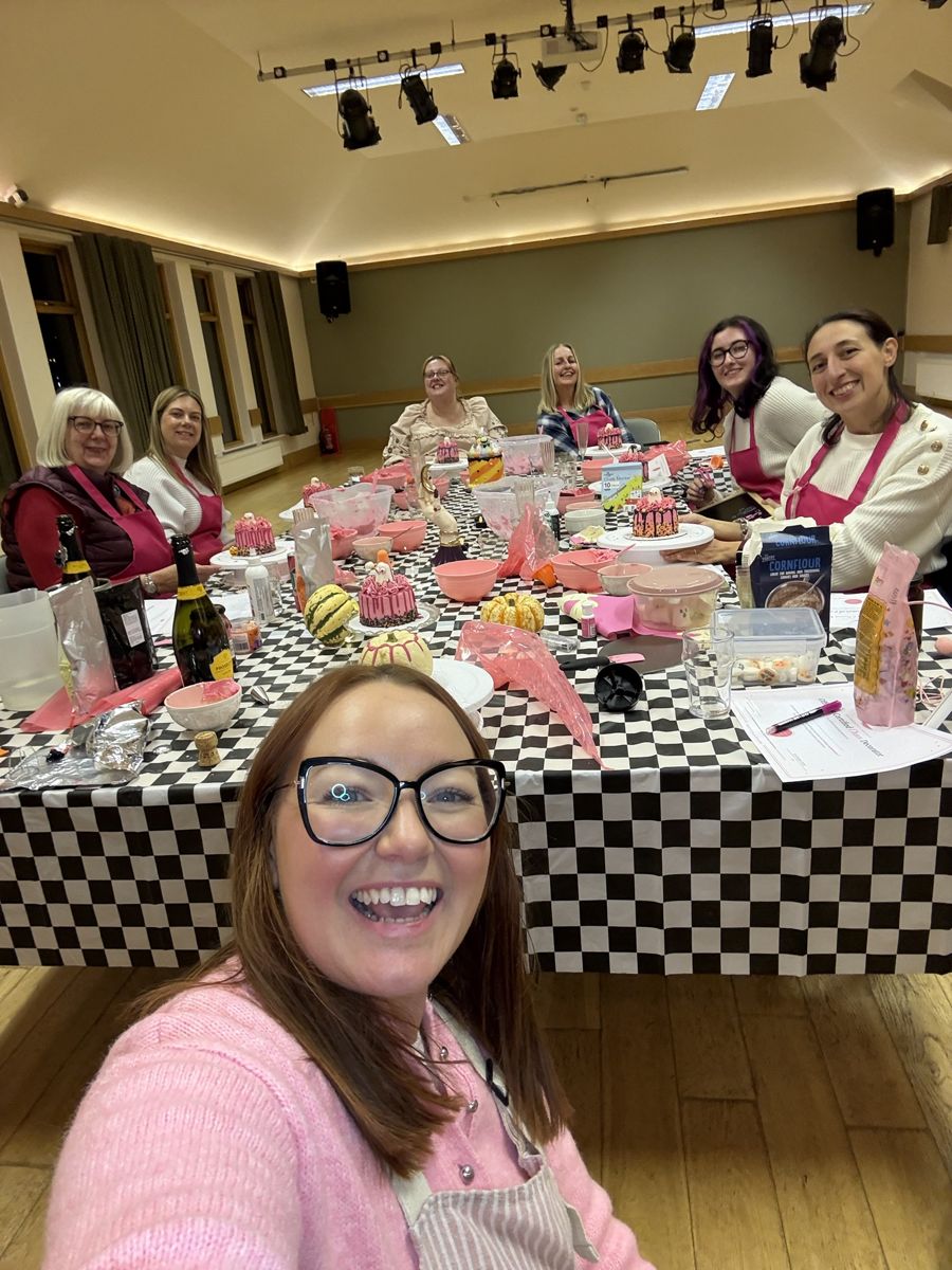 Lauren taking a selfie with six smiling guests in pink aprons at the Halloween Sip and Decorate class