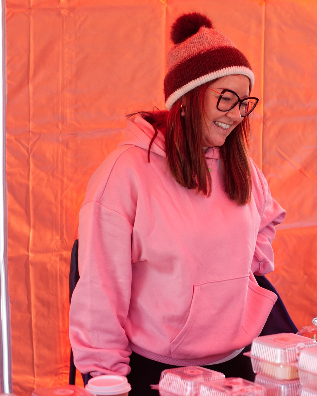 Lauren, owner and baker at Crumb & Chaos Cakes, smiling behind her market stall